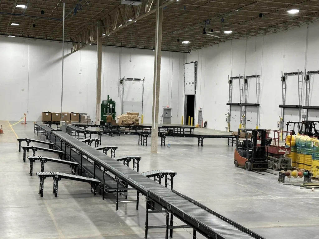 A warehouse with a two level conveyor system. There are four work-stations on each side of the conveyor system. The work stations connect to the lower conveyor level with conveyor ramps.