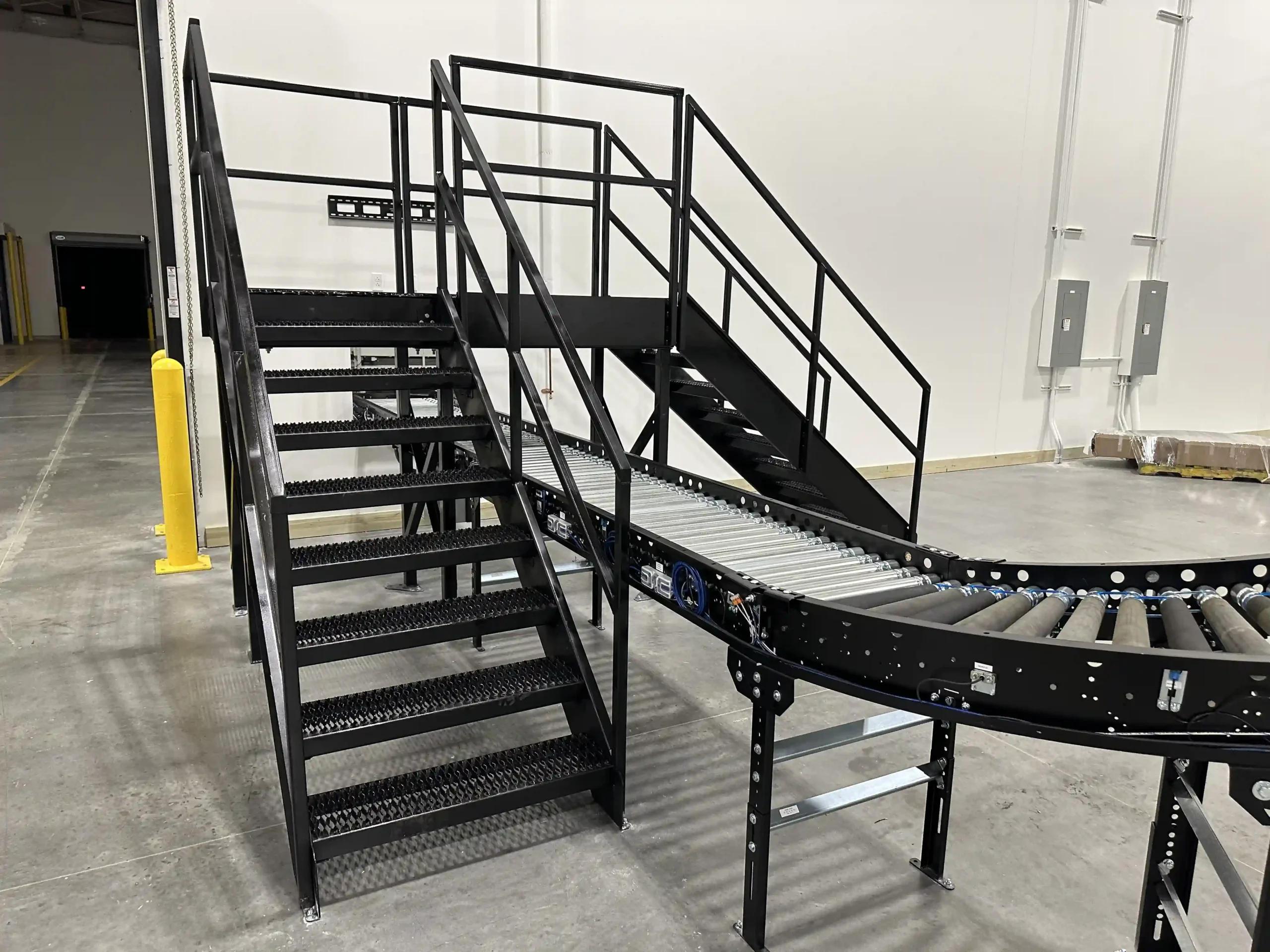 A 3-foot high conveyor with stairs leading up to a crossover 5 feet above the conveyor and another set of stairs on the opposite side of the convey leading down.